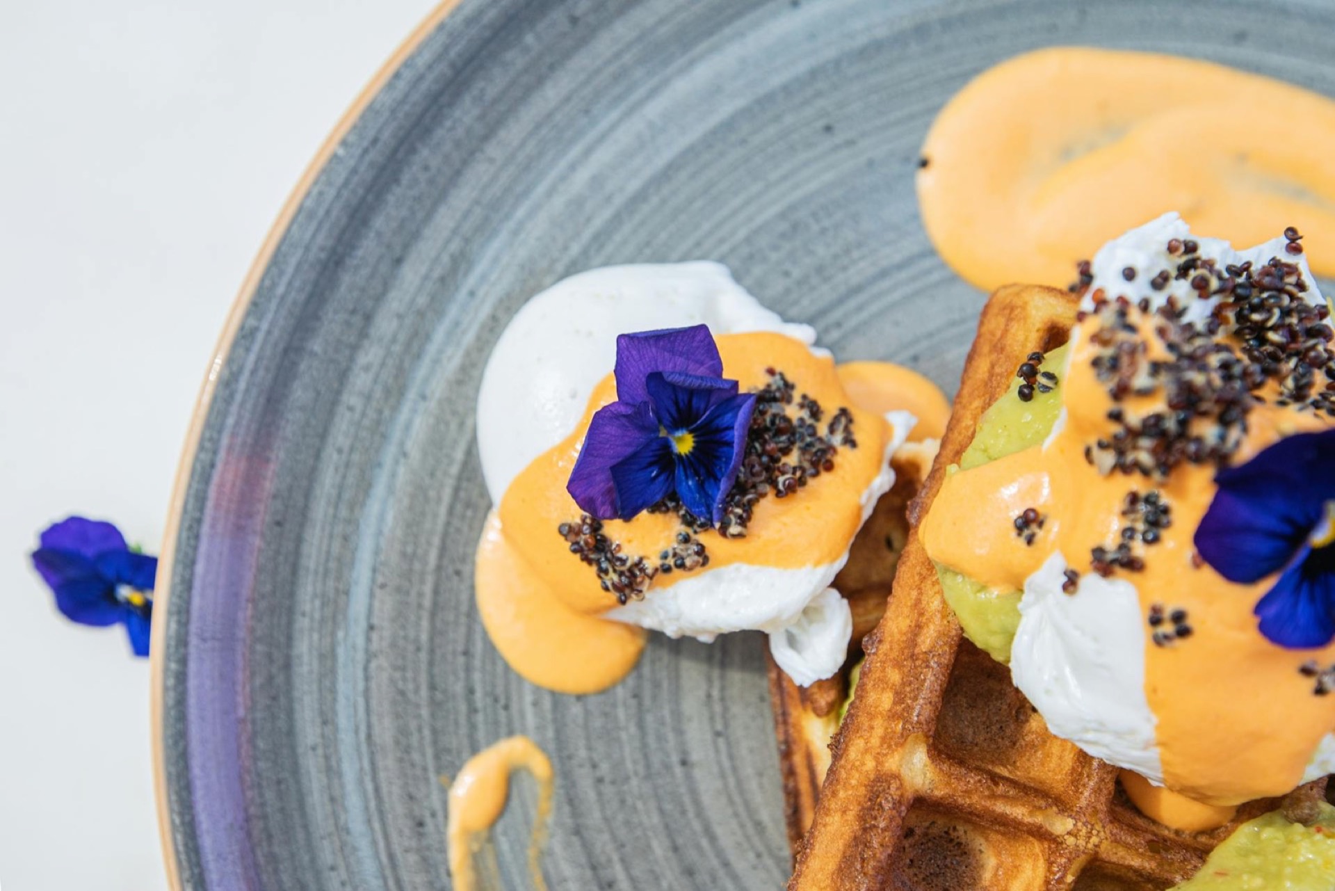 Dessert composé d'une gaufre, crème, pensées violettes et sauce orange — top shot sur assiette céramique