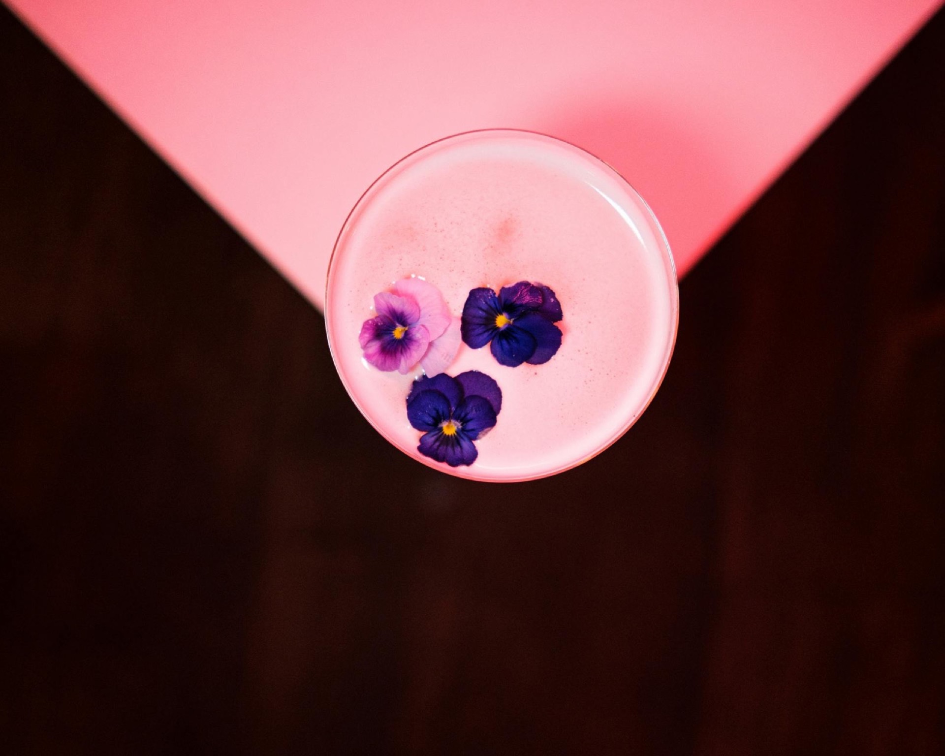Pensées violettes et roses flottant sur un cocktail rose, vue du dessus