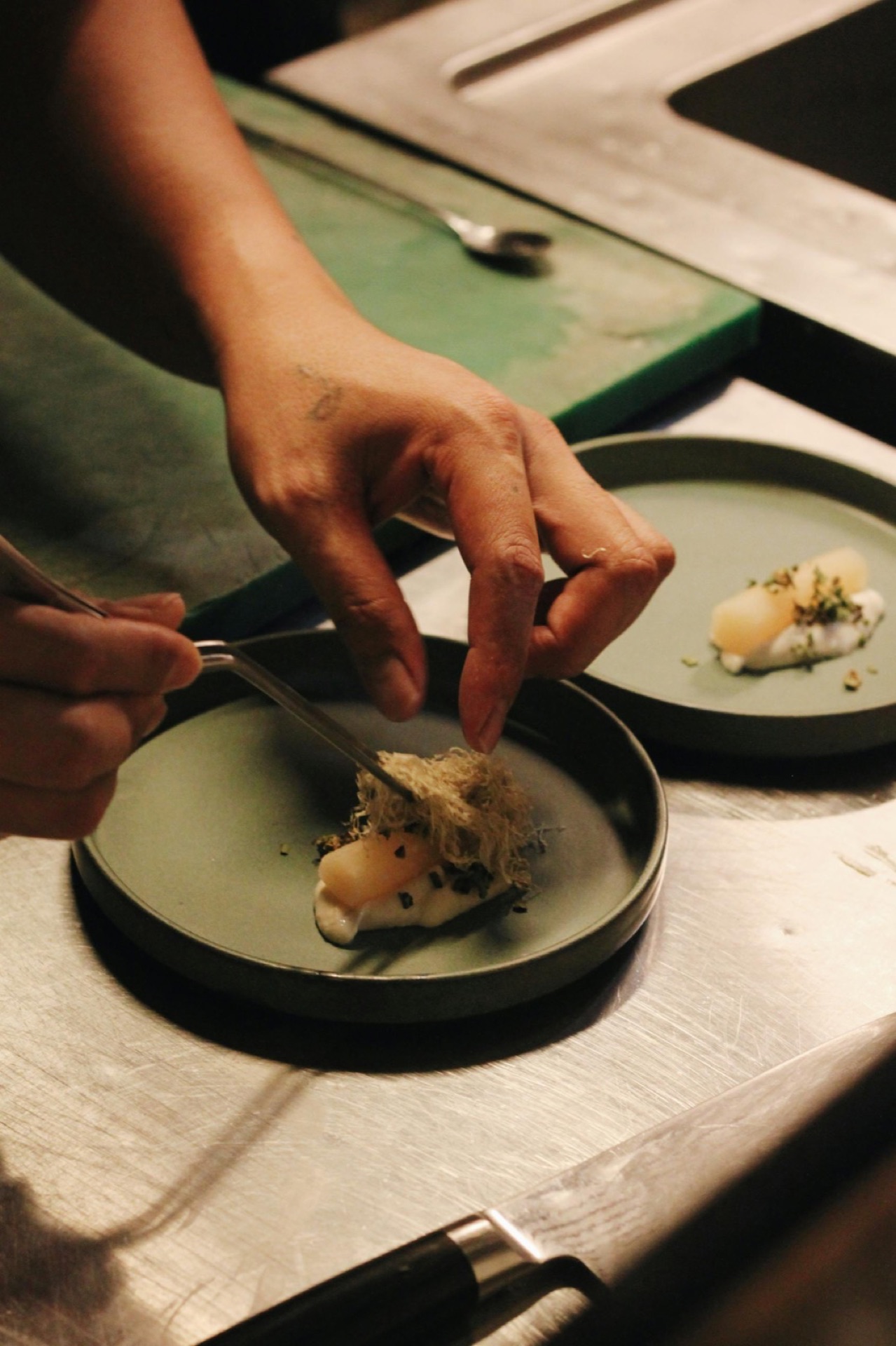 Chef dressant un plat délicat à la pince à épiler sur assiette verte sauge